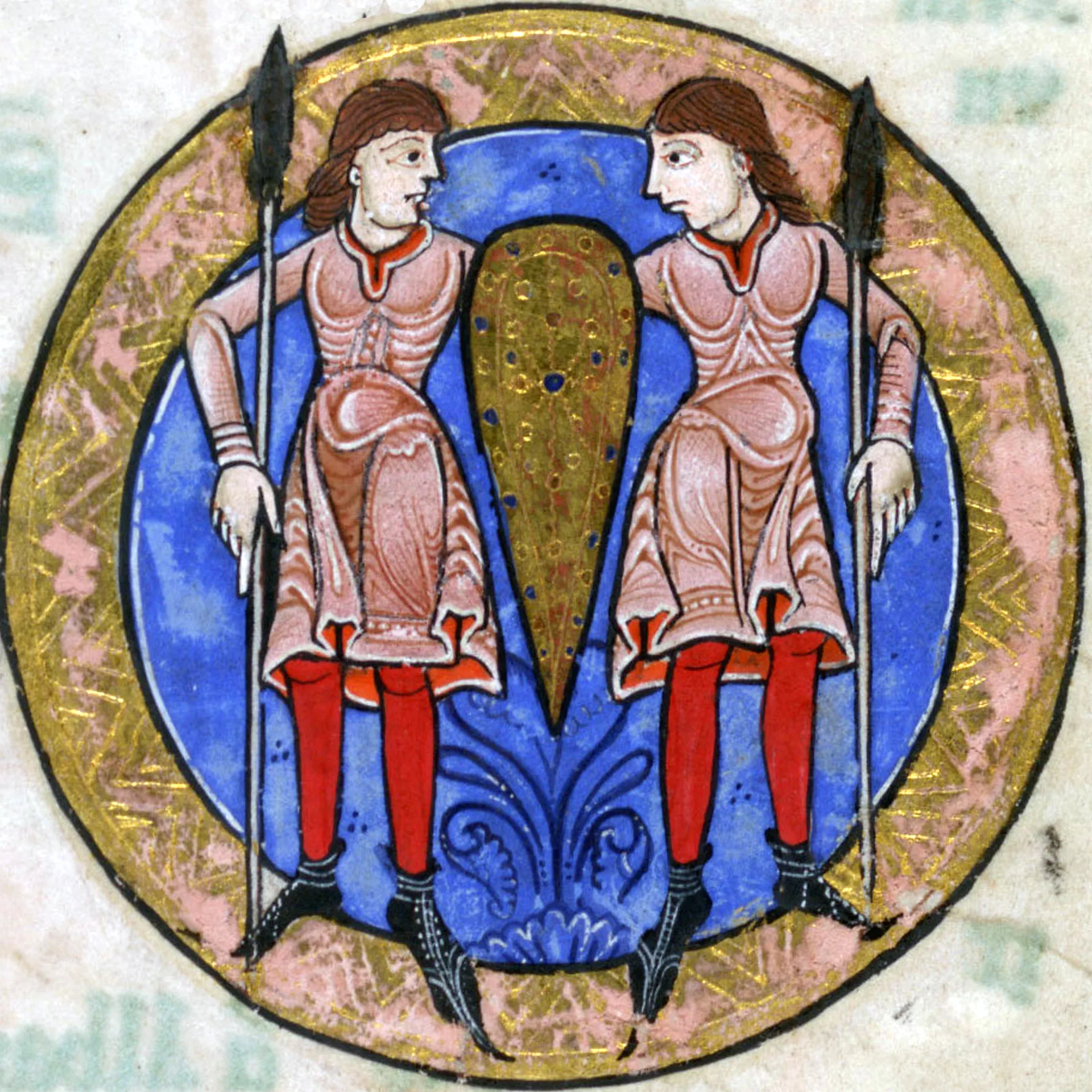 A medieval illuminated manuscript illustration depicts two identical warriors standing side by side within a circular frame outlined in gold. Both figures wear pinkish tunics with intricate white patterns, bright red leggings, and black pointed shoes. They each hold a long spear in one hand and share a single tall, decorated shield placed between them, which is golden with small blue and red dots. Their brown hair is shoulder-length and parted, and they face each other with stern expressions. The background inside the circle is a deep blue with a decorative floral motif at the bottom, surrounded by a pink and gold border.