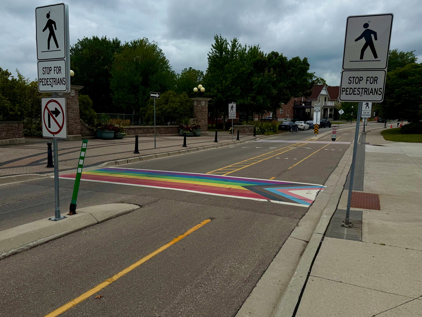 A rainbow-colored crosswalk is situated on a street flanked by signs instructing drivers to stop for pedestrians.